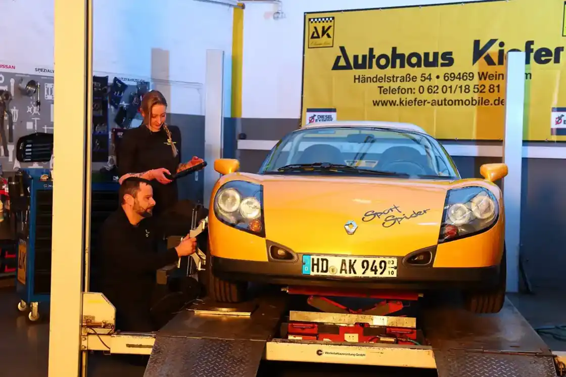 Zwei Mitarbeiter vermessen den gelben Renault Sport Spider auf der Hebebühne