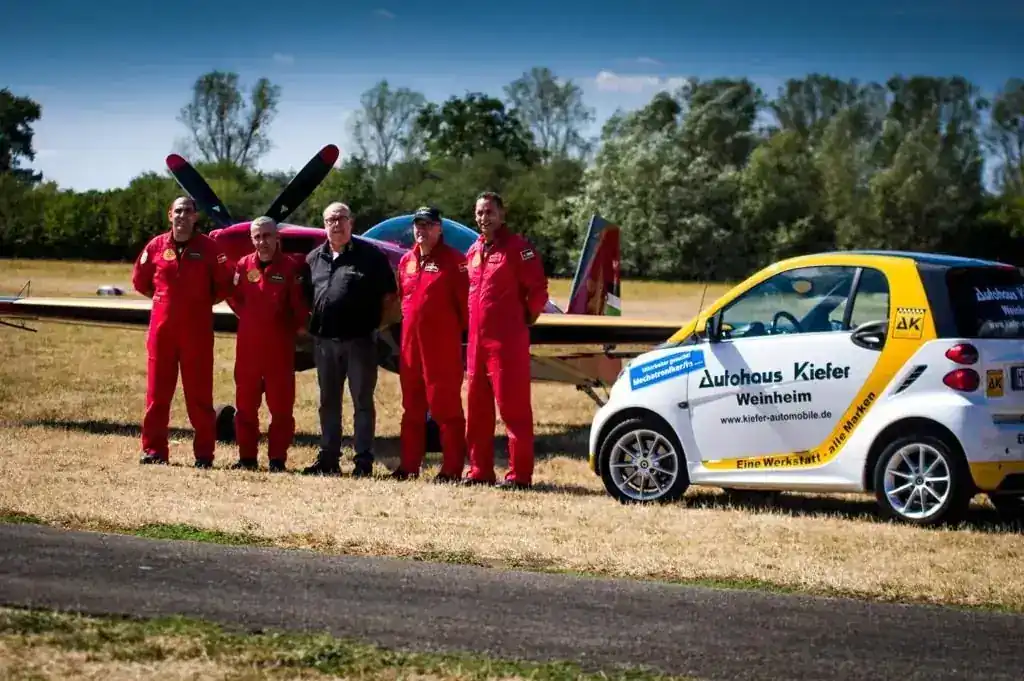 Fahrzeug von Autohaus Kiefer neben einem Kunstflugzeug und Piloten