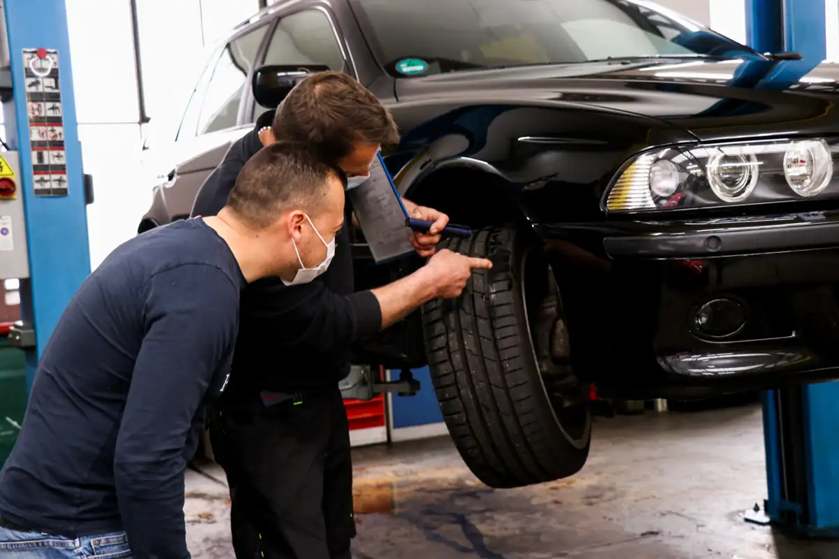 Zwei Mitarbeiter prüfen das Reifenprofil eines Autos